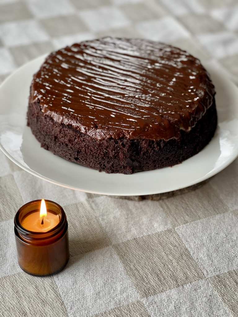 a chocolate cake with chocolate peanut butter icing beside a beeswax candle in a brown apothecary jar